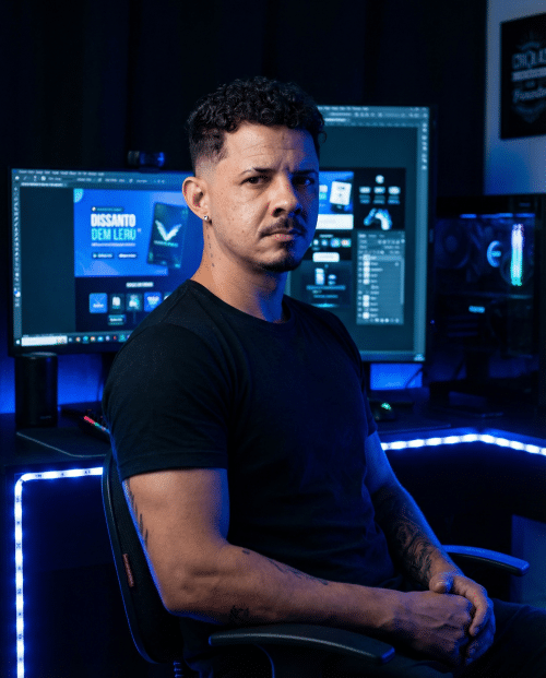 Carlos Salino, designer gráfico, sentado em fundo escuro com iluminação azul RGB